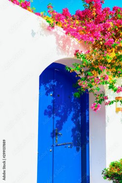 Traditional Mediterranean house with a stone fence and a large blue door decorated with flowering plants