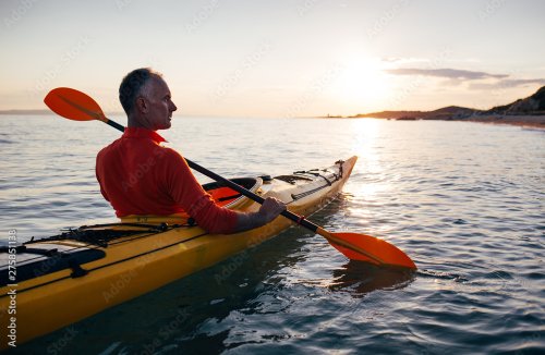 Senior man paddling kayak on the sunset sea